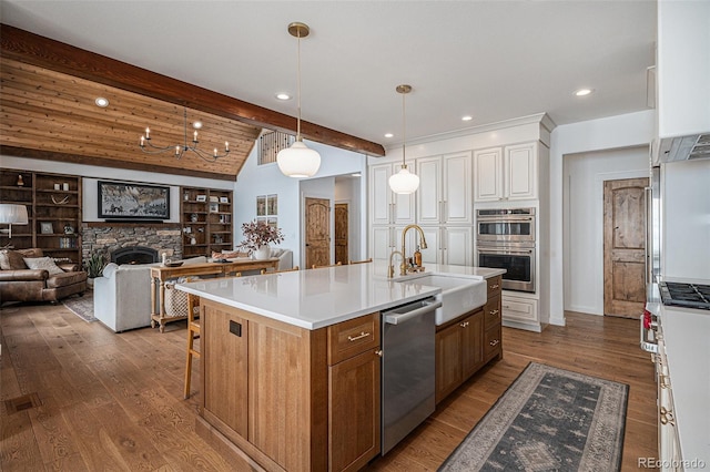 kitchen with appliances with stainless steel finishes, white cabinetry, sink, hanging light fixtures, and a center island with sink