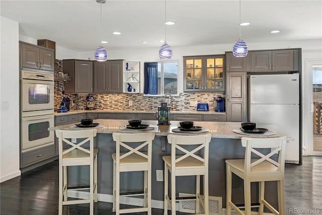 kitchen featuring light stone countertops, decorative light fixtures, white appliances, a breakfast bar, and a kitchen island