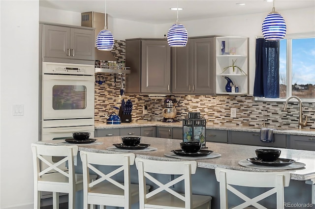 kitchen with backsplash, decorative light fixtures, gray cabinetry, and a breakfast bar area