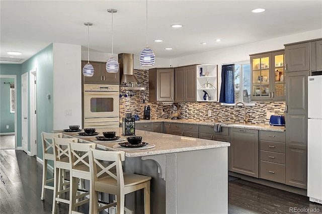 kitchen featuring a center island, dark wood-type flooring, wall chimney exhaust hood, and hanging light fixtures