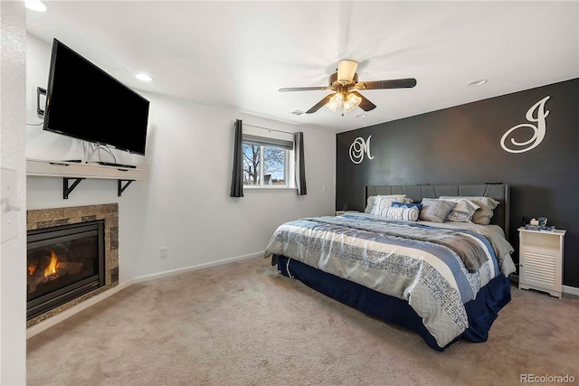 bedroom featuring a tile fireplace, ceiling fan, and light carpet