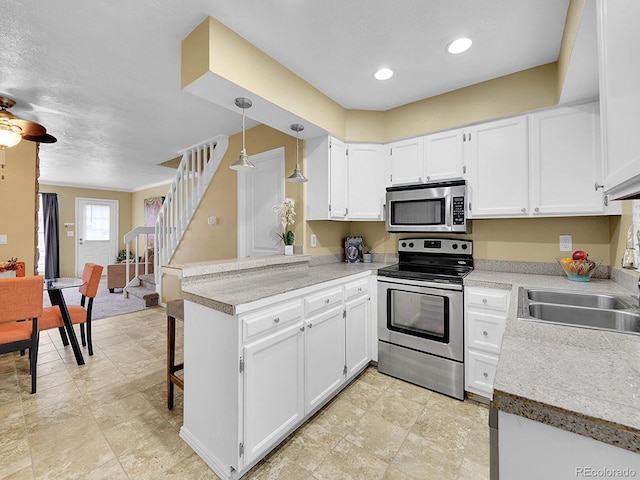 kitchen with decorative light fixtures, stainless steel appliances, kitchen peninsula, and white cabinets