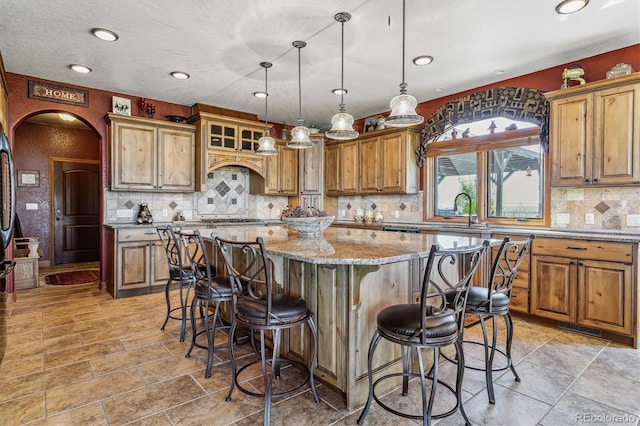 kitchen with a kitchen bar, light stone counters, sink, pendant lighting, and a center island