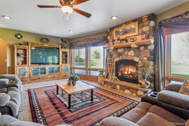 living room featuring a stone fireplace, ceiling fan, and a textured ceiling