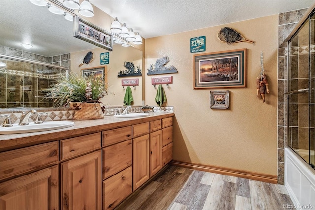 bathroom with hardwood / wood-style floors, vanity, enclosed tub / shower combo, and a textured ceiling