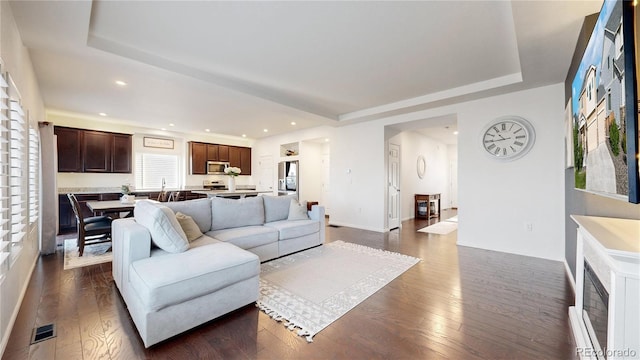 living room with a tray ceiling, dark wood-style flooring, visible vents, and recessed lighting