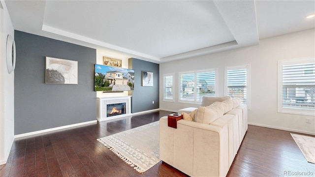 living room featuring baseboards, a raised ceiling, dark wood-style flooring, and a glass covered fireplace