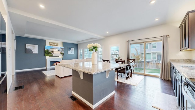 kitchen featuring dark wood-style floors, light stone counters, visible vents, a lit fireplace, and a kitchen breakfast bar