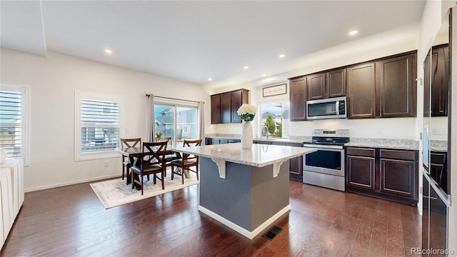 kitchen featuring dark brown cabinetry, appliances with stainless steel finishes, a kitchen breakfast bar, and dark wood-style flooring