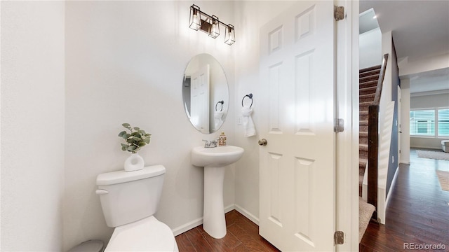 half bath featuring wood finished floors, toilet, and baseboards