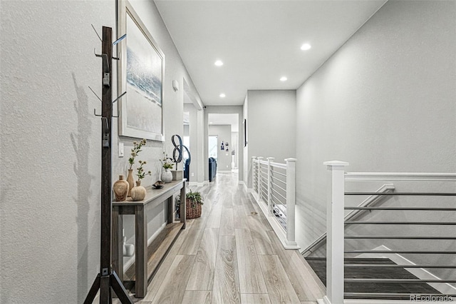 hall with an upstairs landing, a textured wall, light wood-style floors, and recessed lighting