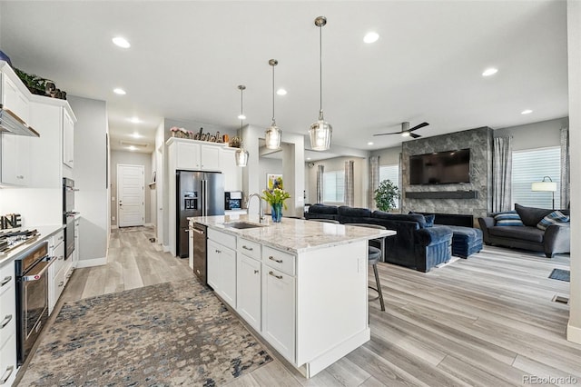 kitchen with white cabinets, a sink, light wood-type flooring, a kitchen island with sink, and ceiling fan