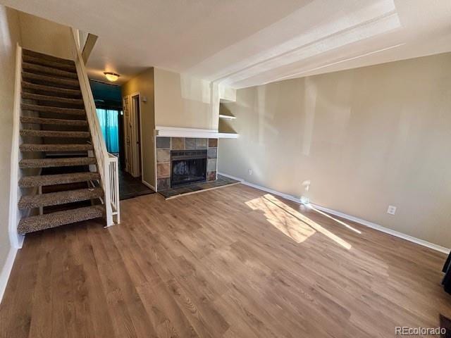 unfurnished living room featuring baseboards, stairway, a tiled fireplace, and wood finished floors