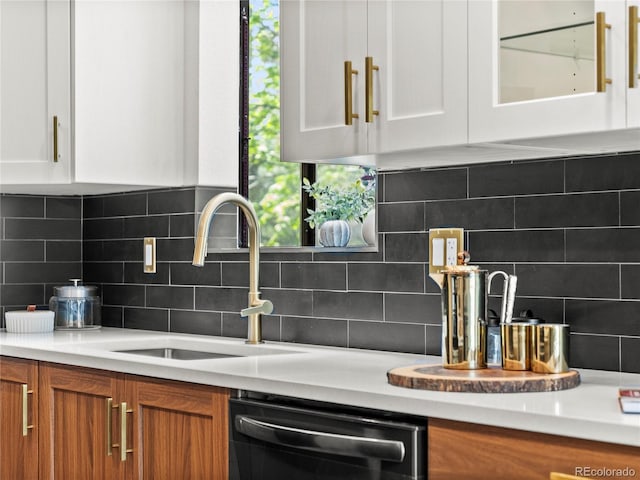 kitchen featuring dishwasher, a sink, white cabinets, light countertops, and decorative backsplash
