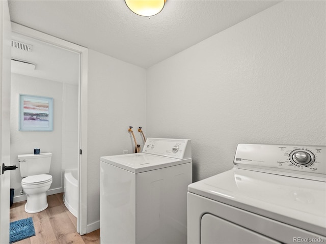 clothes washing area featuring washing machine and clothes dryer, light wood finished floors, and a textured ceiling
