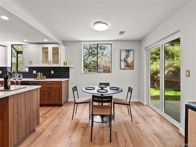 kitchen with light countertops, light wood-style flooring, glass insert cabinets, backsplash, and recessed lighting