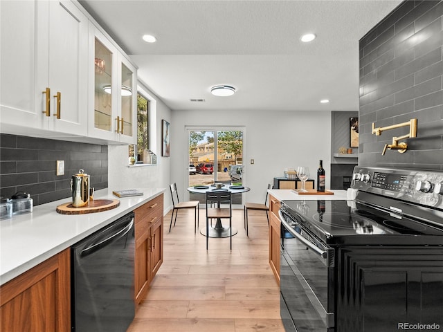 kitchen with black appliances, light countertops, glass insert cabinets, brown cabinetry, and light wood-style flooring