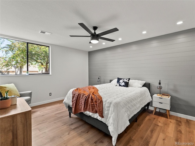 bedroom featuring baseboards, light wood-type flooring, recessed lighting, a ceiling fan, and wood walls
