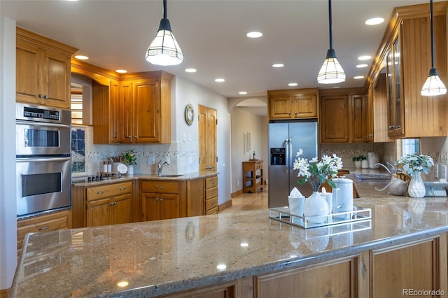 kitchen featuring hanging light fixtures, light stone countertops, kitchen peninsula, and appliances with stainless steel finishes