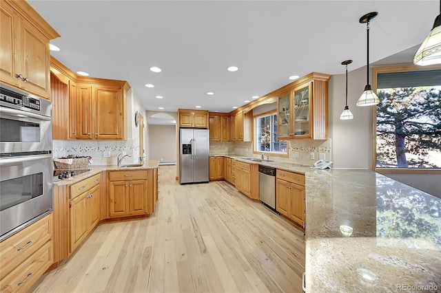 kitchen featuring tasteful backsplash, light stone counters, pendant lighting, stainless steel appliances, and light hardwood / wood-style floors