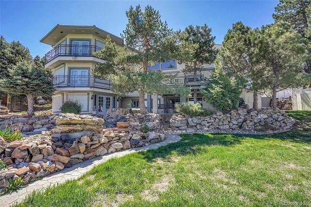 rear view of property with a balcony, french doors, stucco siding, and a lawn