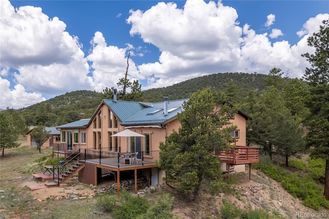1111 Red Feather Rd, Cotopaxi, CO 81223 - rear view of house featuring a deck with mountain view, stucco siding, stairs, metal roof, and a view of trees