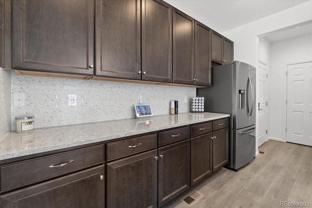 kitchen with light stone counters, backsplash, dark brown cabinetry, and light wood-type flooring