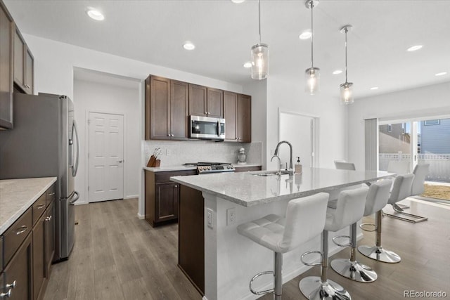 kitchen featuring dark brown cabinetry, an island with sink, appliances with stainless steel finishes, pendant lighting, and a sink