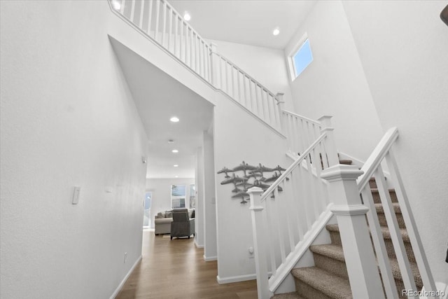 staircase with plenty of natural light, baseboards, a towering ceiling, and wood finished floors