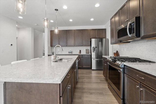 kitchen with an island with sink, a sink, dark wood-style floors, appliances with stainless steel finishes, and dark brown cabinets