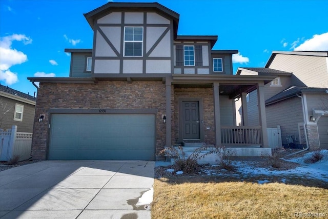 tudor home featuring stucco siding, driveway, fence, covered porch, and an attached garage