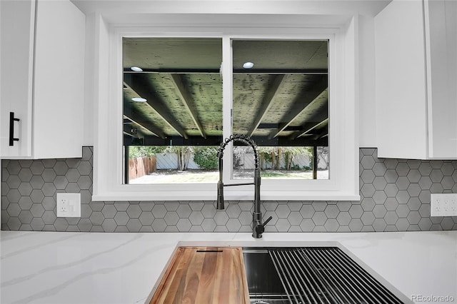 interior details featuring decorative backsplash, light stone countertops, and white cabinets