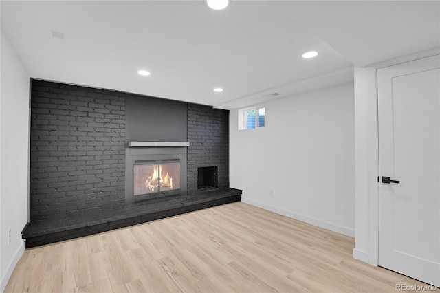 unfurnished living room with light wood-type flooring and a brick fireplace