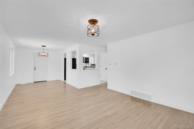 unfurnished living room featuring a chandelier and light hardwood / wood-style flooring