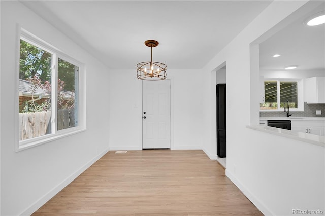 unfurnished dining area with light wood-type flooring and a notable chandelier