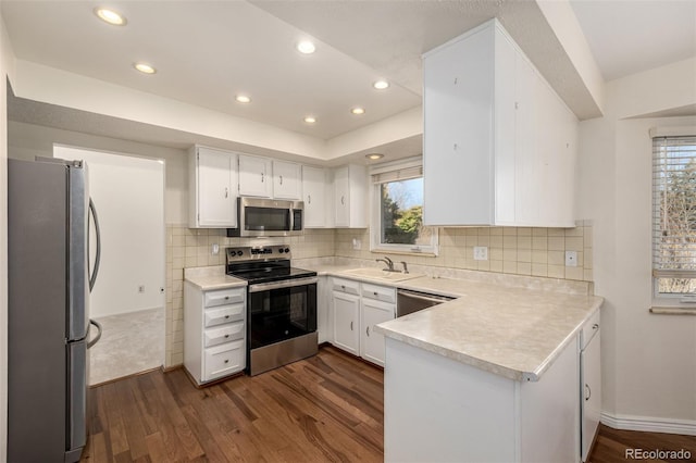 kitchen with appliances with stainless steel finishes, light countertops, dark wood finished floors, and a peninsula