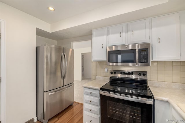 kitchen with white cabinetry, light countertops, appliances with stainless steel finishes, decorative backsplash, and light wood finished floors