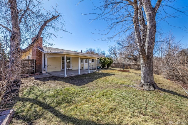 rear view of house featuring a chimney, fence, a lawn, and a patio