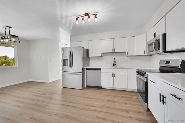 2503-2507 N Taft Ave, Loveland, CO 80538 - kitchen featuring appliances with stainless steel finishes, decorative backsplash, white cabinets, light wood finished floors, and hanging light fixtures