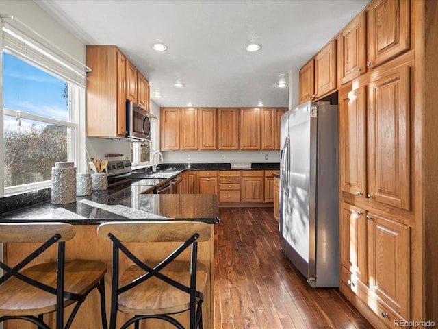 kitchen with recessed lighting, stainless steel appliances, a peninsula, a kitchen breakfast bar, and dark wood-style floors