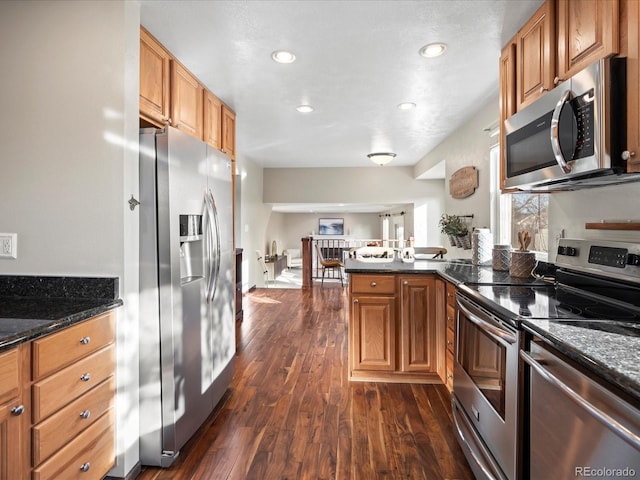 kitchen featuring brown cabinetry, appliances with stainless steel finishes, open floor plan, dark wood-type flooring, and a peninsula