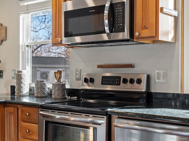 kitchen featuring dark stone counters, stainless steel appliances, and brown cabinets