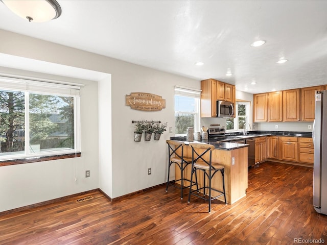 kitchen with a peninsula, a breakfast bar, visible vents, appliances with stainless steel finishes, and dark wood finished floors