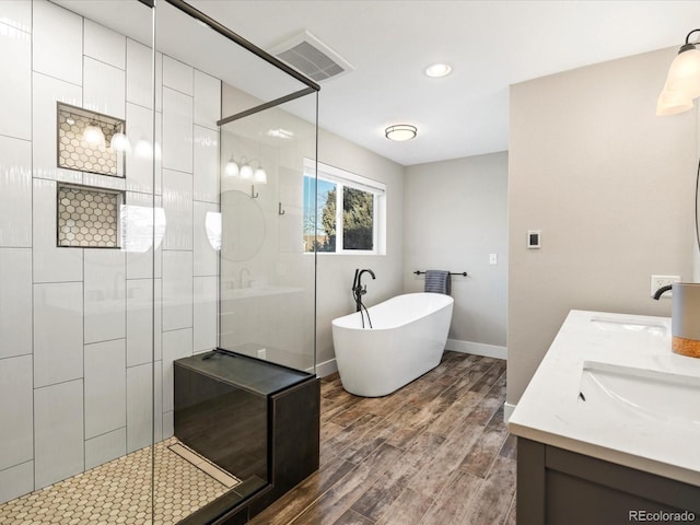 bathroom featuring visible vents, wood finished floors, a tile shower, a freestanding bath, and a sink