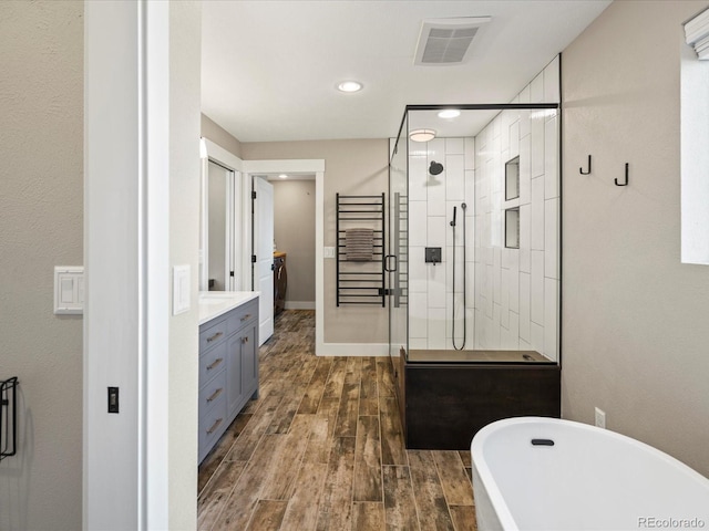 full bath featuring a freestanding tub, wood finished floors, vanity, visible vents, and a shower stall