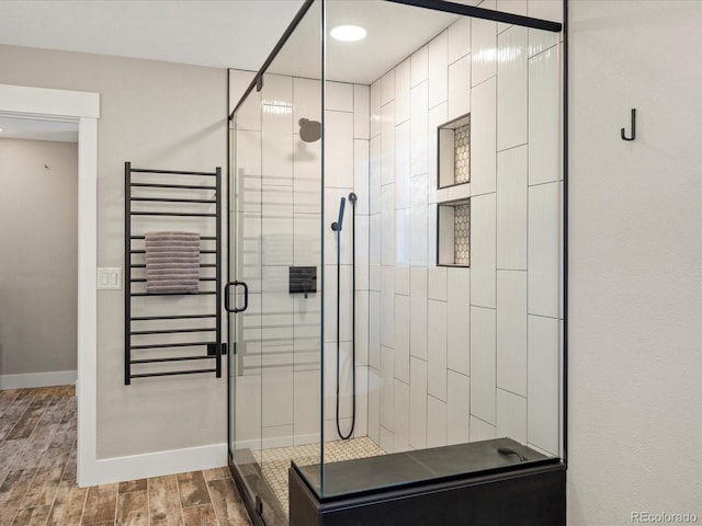 bathroom featuring a stall shower, radiator, baseboards, and wood finished floors