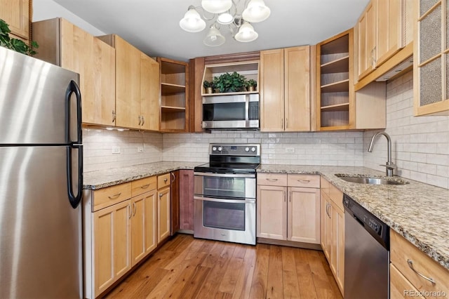 kitchen featuring appliances with stainless steel finishes, backsplash, light stone counters, sink, and light hardwood / wood-style floors