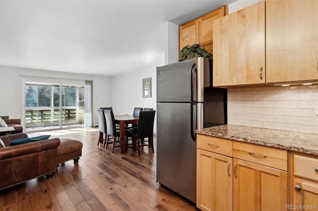 kitchen featuring light brown cabinets, backsplash, dark wood-type flooring, light stone counters, and stainless steel refrigerator