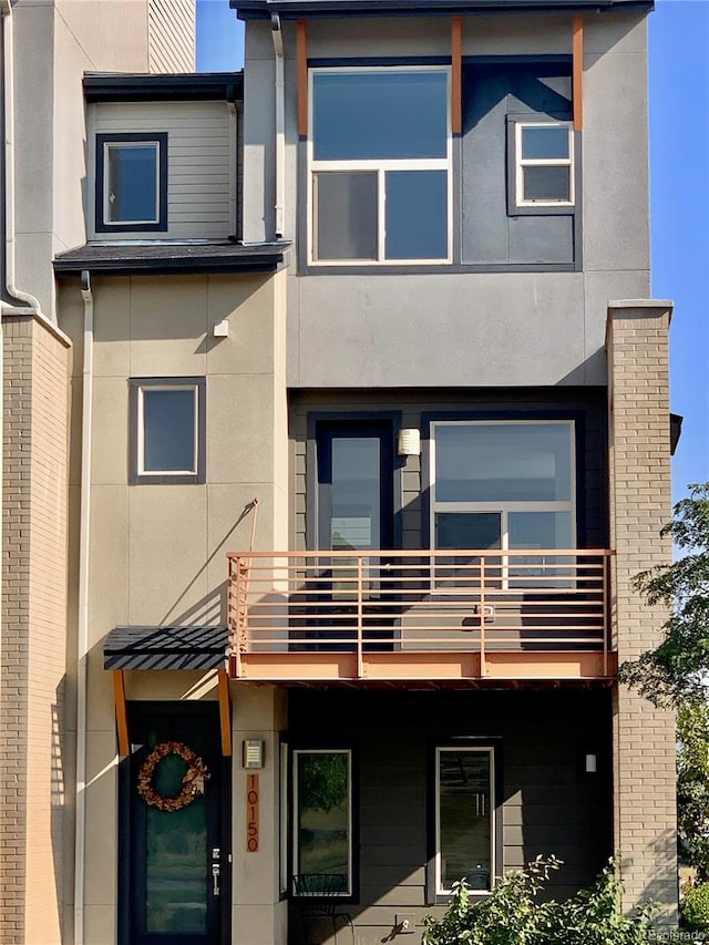 rear view of house with a balcony and stucco siding