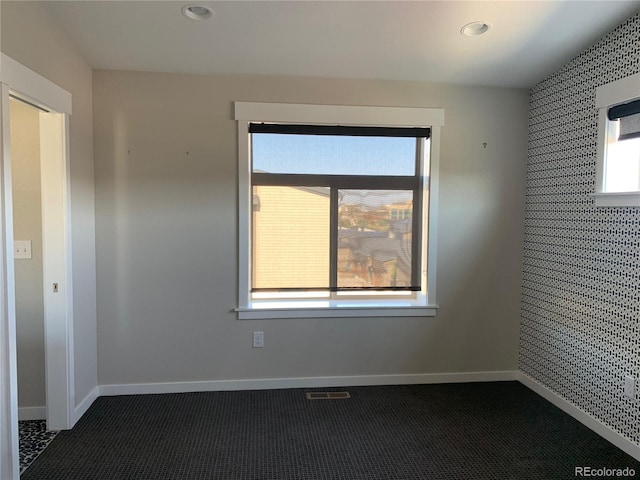 spare room with baseboards, visible vents, dark colored carpet, and a wealth of natural light